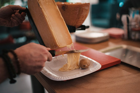 Geschmolzener Raclettekäse wird auf ein Holzbrett geschabt – welcher Wein passt zu Raclette