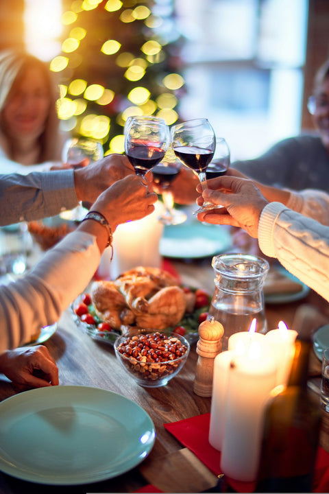 Festlich gedeckter Tisch, Gäste stoßen mit Rotwein an – der passende Wein zum Weihnachtsessen